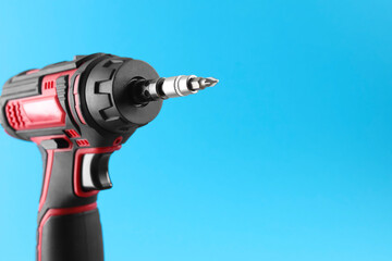 Modern electric screwdriver on light blue background, closeup. Space for text