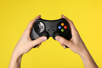 Woman using game controller on yellow background, closeup