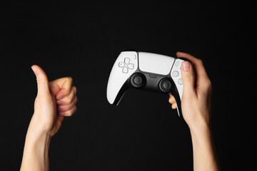 Woman with game controller showing thumbs up on black background, closeup © New Africa
