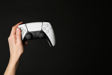 Woman holding game controller on black background, closeup. Space for text