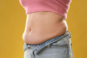 Woman with excessive belly fat on goldenrod background, closeup. Overweight problem