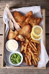 Tasty fish, chips, sauce and peas on wooden table, top view