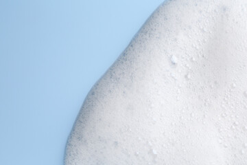 White fluffy foam on light blue background, top view. Space for text