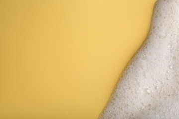 White fluffy foam on yellow background, top view. Space for text