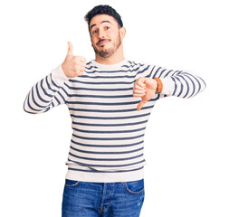 Naklejka premium Young hispanic man wearing casual clothes doing thumbs up and down, disagreement and agreement expression. crazy conflict