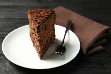 Piece of delicious chocolate truffle cake and fork on black wooden table, closeup