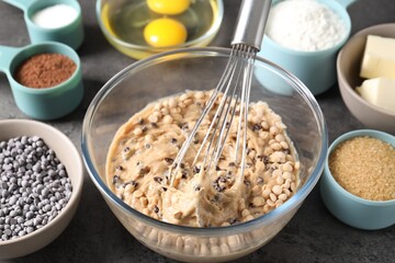 Raw dough with chocolate chips in bowl and ingredients on grey table, closeup