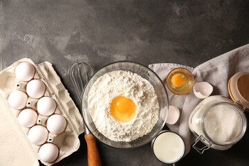 Making dough. Flour with egg yolk in bowl and other products on grey textured table, flat lay