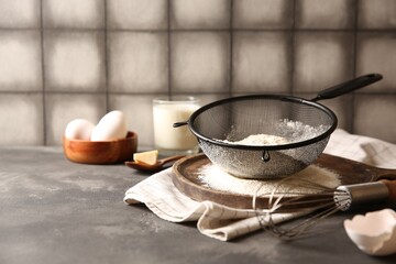Flour in sieve and other ingredients for dough on grey textured table, closeup. Space for text