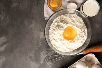 Making dough. Flour with egg yolk in bowl and other products on grey textured table, flat lay. Space for text