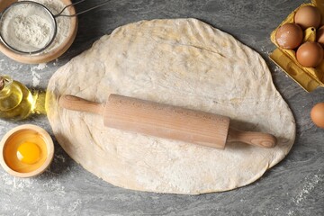 Raw dough, rolling pin and ingredients on grey table, flat lay