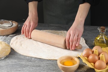 Woman rolling raw dough at grey table, closeup