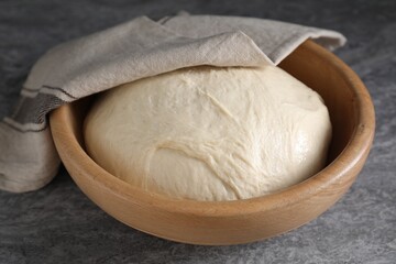 Raw dough in bowl on grey table, closeup