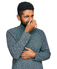 Young african american man wearing casual clothes smelling something stinky and disgusting, intolerable smell, holding breath with fingers on nose. bad smell