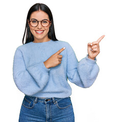 Young hispanic woman wearing casual clothes and glasses smiling and looking at the camera pointing...