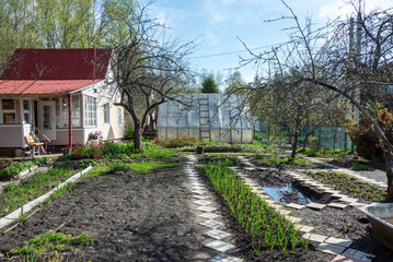 A summer house, vegetable beds with fruit trees and a greenhouse in early spring.