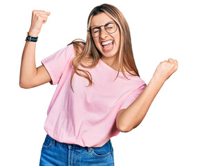 Hispanic young woman wearing casual t shirt and glasses very happy and excited doing winner gesture...