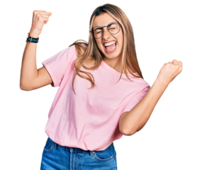 Hispanic young woman wearing casual t shirt and glasses very happy and excited doing winner gesture with arms raised, smiling and screaming for success. celebration concept.