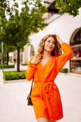 Beautiful young woman wearing nice orange dress walking on the street. Concept of lifestyle, fashion, travel.