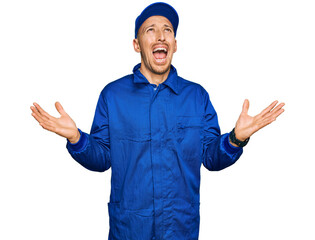 Bald man with beard wearing builder jumpsuit uniform crazy and mad shouting and yelling with...