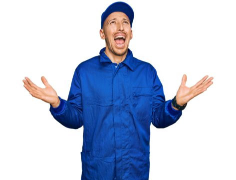Bald man with beard wearing builder jumpsuit uniform crazy and mad shouting and yelling with aggressive expression and arms raised. frustration concept.