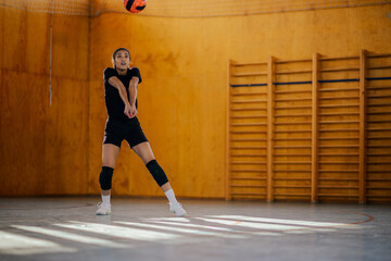 Woman playing volleyball in a sports hall and passing the ball with a bump