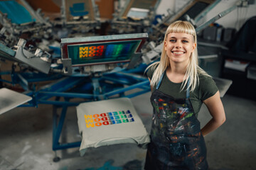 Happy print shop worker standing near screen printing press and smiling