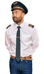 Handsome man with beard wearing airplane pilot uniform smiling looking to the side and staring away thinking. © Krakenimages.com