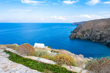 View of small chapel overlooking sea bay and rocky coast cliffs from Kastro village, Sifnos island,...