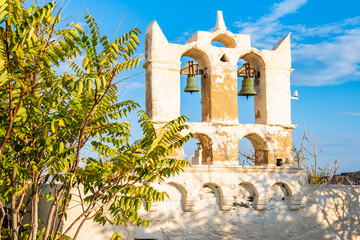 Facade of Greek church framed with green tree leaves on street of Kastro village at sunset, Sifnos...