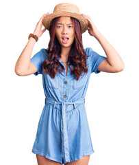 Young beautiful chinese girl wearing summer hat crazy and scared with hands on head, afraid and surprised of shock with open mouth