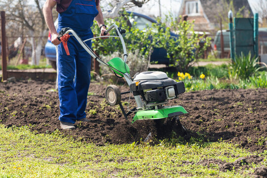 A farmer in the garden tills the land with a motorized cultivator or power tiller, preparing the soil for planting crops