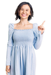 Young beautiful girl wearing casual clothes with a big smile on face, pointing with hand finger to the side looking at the camera.