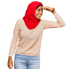 Young african american woman wearing traditional islamic hijab scarf very happy and smiling looking far away with hand over head. searching concept.