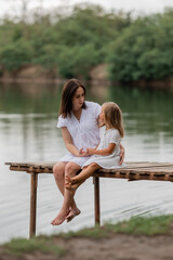 Mom and daughter sit on a wooden lake bridge in summer, Mother's Day