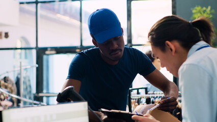 Asian manager signing delivery report, discussing shipping details with african american courier in...