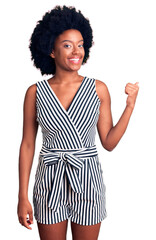 Young african american woman wearing casual clothes smiling with happy face looking and pointing to the side with thumb up.