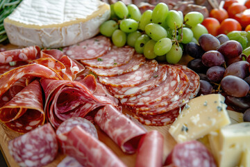 Delicious charcuterie board with various kinds of cured meat, cheese, vegetables, olives and other accompaniments