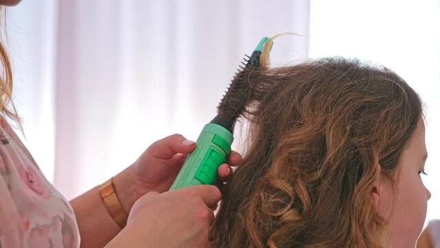 Caucasian Woman using Electric Curling Hairdryer Doing a Hairstyle for Teenage Girl Before Debutante Ceremony or School Prom Party 