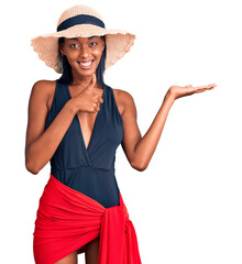 Young african american woman wearing swimsuit and summer hat showing palm hand and doing ok gesture with thumbs up, smiling happy and cheerful