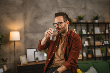 Portrait of adult caucasian man sit and drink glass of water at home