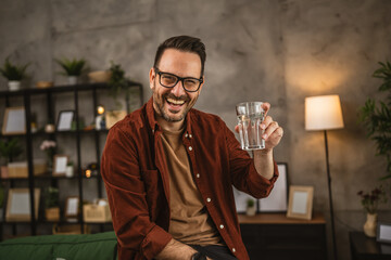 Portrait of adult caucasian man sit and hold glass of water at home