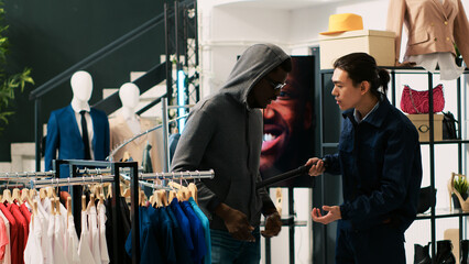 Robber wearing hood and sunglasses while trying to stole fashionable clothes in modern boutique....