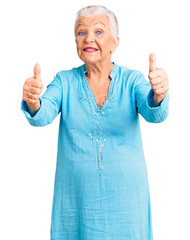 Senior beautiful woman with blue eyes and grey hair wearing summer dress approving doing positive gesture with hand, thumbs up smiling and happy for success. winner gesture.