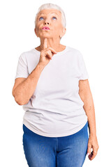 Senior beautiful woman with blue eyes and grey hair wearing casual white tshirt thinking concentrated about doubt with finger on chin and looking up wondering