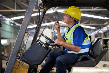 senior worker using walkie talkie and driving forklift truck in the factory