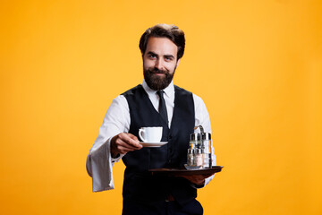 Elegant butler giving coffee cup to clients, pretending to serve people while he holds platter with...