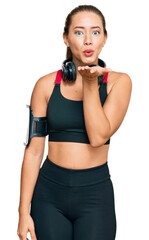 Beautiful blonde woman wearing gym clothes and using headphones looking at the camera blowing a kiss with hand on air being lovely and sexy. love expression.