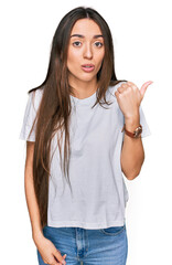 Young hispanic girl wearing casual white t shirt surprised pointing with hand finger to the side, open mouth amazed expression.