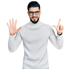 Fototapeta premium Young arab man with beard wearing elegant turtleneck sweater and glasses showing and pointing up with fingers number seven while smiling confident and happy.
